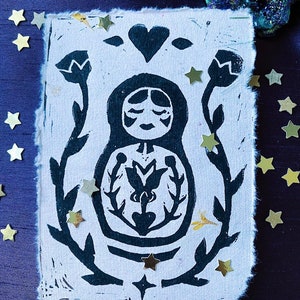 Könnte beinhalten: Ein Schwarz-Weiß-Linolschnitt einer stilisierten Frau mit einem Herzen über ihrem Kopf. Die Frau ist von floralen Mustern und Sternen umgeben.