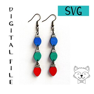 Può includere: Orecchini pendenti con un design a luci natalizie. Ogni orecchino ha tre luci in legno blu, verdi e rosse, collegate da metallo color argento. Gli orecchini sono sospesi da ganci per le orecchie color bronzo. L'immagine include anche il testo "DIGITAL FILE" e "SVG".