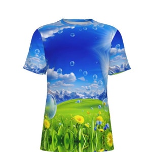 Puede incluir: Una camiseta azul y verde con un estampado gráfico de un campo de hierba, flores y montañas con burbujas de jabón flotando en el cielo.