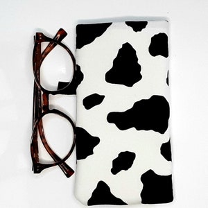 May include: A black and white cow print glasses case with a brown pair of glasses next to it.