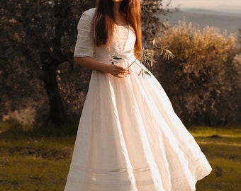 May include: A cream-colored midi dress featuring elbow-length sleeves, a fitted bodice with lace detailing, and a full, flared skirt with horizontal lace trim and a scalloped hemline, paired with dark brown lace-up boots.