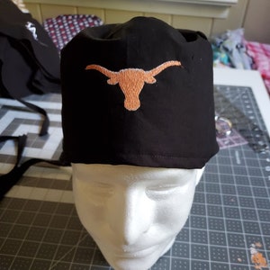 May include: Black scrub hat with a burnt orange embroidered Longhorn steer head logo.