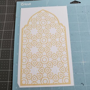 May include: A white cardstock sheet with a beige geometric design cut out. The design features a repeating pattern of stars and hexagons.