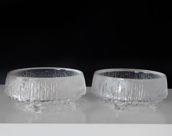 May include: Two clear glass bowls with a textured surface and three legs each. The bowls are on a white surface.