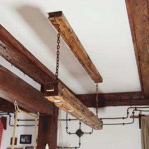 A wooden beam lamp hanging on chains in a rustic style with a long ceiling lining. A unique wooden lamp with halogen lamps, loft/rustic.