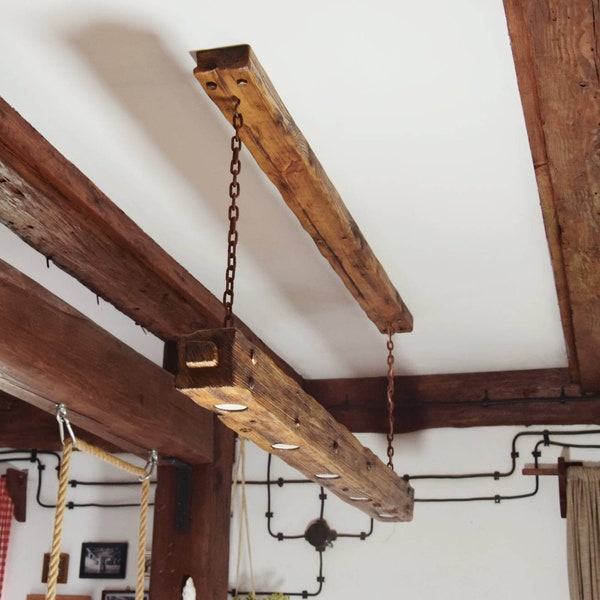 A rustic wooden beam lamp hanging on chains with a long canopy. A unique wooden lamp with halogen lights in a loft/rustic style.