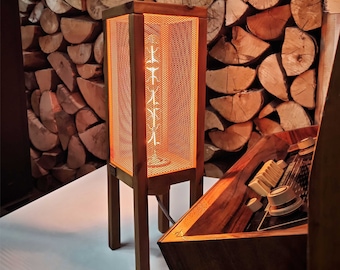 May include: A wooden table lamp with a wire mesh shade and a warm orange glow. The lamp is on a white surface and has a wooden base.