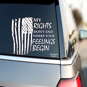 May include: White vinyl decal with a distressed American flag and the text "My Rights Don't End Where Your Feelings Begin". The decal is on the back window of a silver car. The text "Forevermore Graphics" is at the bottom of the decal.