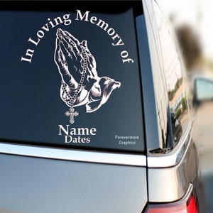 May include: White vinyl decal with a pair of praying hands holding a rosary and a cross. The decal reads "In Loving Memory of" and has space for a name and dates.