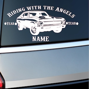 May include: White car decal with the text "RIDING WITH THE ANGELS" above a classic car illustration. Includes spaces for "YEAR" and "NAME" in a vintage font. The decal is designed to be applied to a car window.