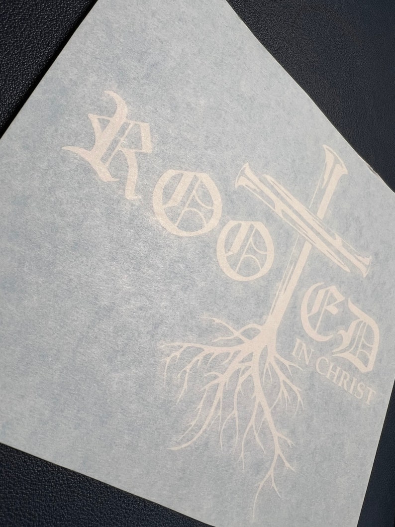 K&ouml;nnte beinhalten: Wei&szlig;er Vinyl-Aufkleber mit dem Wort "Rooted" in einer stilisierten Schriftart, einem Kreuz und einem Baumwurzel-Design. Der Text "In Christ" befindet sich unter den Baumwurzeln.