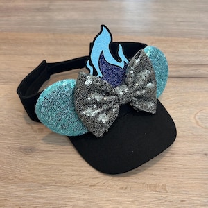 May include: A black visor with a blue and purple flame design, a silver sequined bow, and turquoise sequined ears.
