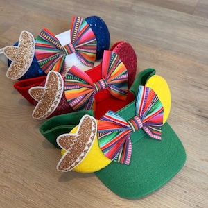 May include: A collection of colorful visors with festive designs. Each visor features a vibrant, striped bow and a decorative element, including a glittery sombrero. The visors come in various colors, including red, green, blue, and yellow.