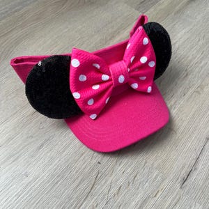 May include: Pink sun hat with a white polka dot bow and black sequin ears.