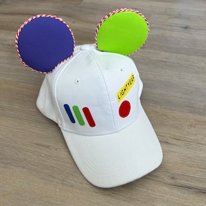 May include: White baseball cap with red, blue, green, and yellow stripes and a red circle. The cap has two fabric ears, one purple and one green, attached to the top. The text "LIGHTYEAR" is on the cap.