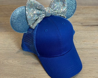 May include: A blue baseball cap with a mesh back and a silver glitter bow on top. The bow is attached to two blue glitter ears.