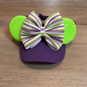 May include: Purple baseball cap with a green and white striped bow and green fuzzy ears.