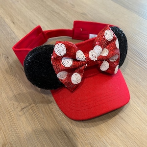 May include: Red visor with a large red and white polka dot bow and black sequin mouse ears.
