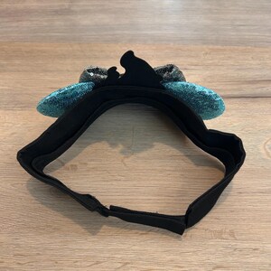 May include: A black headband with turquoise sequin ears. The headband is made of a soft, stretchy material and is designed to fit comfortably on the head.