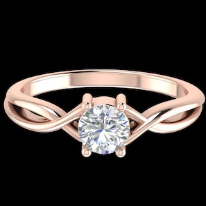 Peut inclure: Bague de fiançailles en or rose avec une pierre précieuse ronde et transparente. Le bracelet présente un design torsadé qui se fond dans le sertissage, créant un look élégant. La bague est sur fond noir.