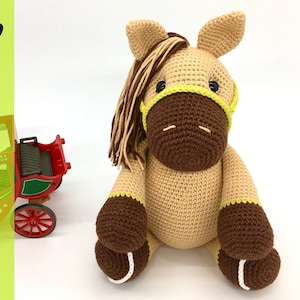 May include: A crocheted brown and tan horse with a yellow and green bridle. The horse is sitting with its legs crossed and has a brown mane.
