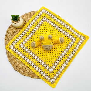 May include: A yellow and white crocheted baby blanket with a brown and yellow crocheted giraffe toy in the centre.