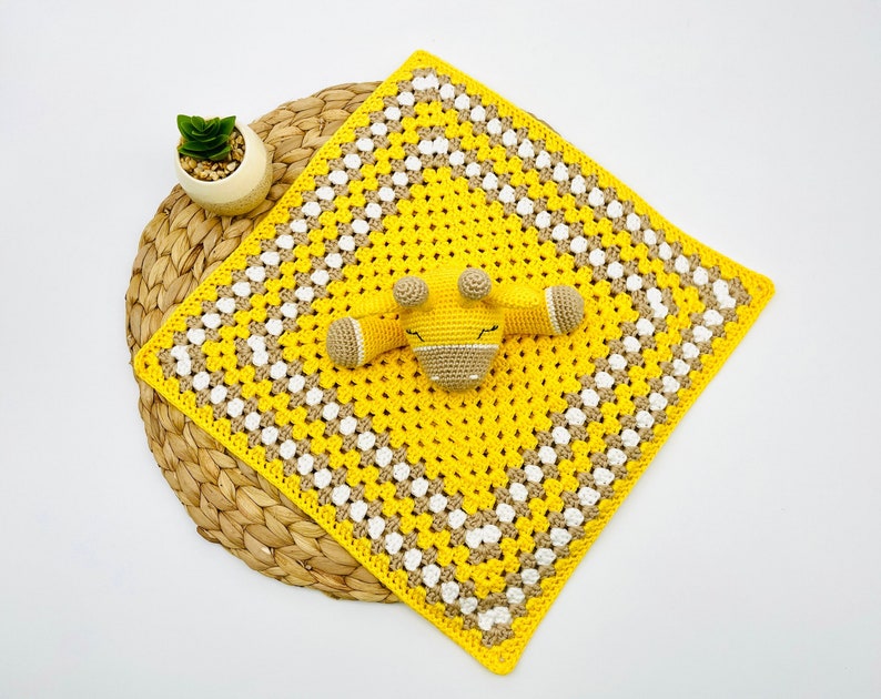 May include: A yellow and white crocheted baby blanket with a brown and yellow crocheted giraffe toy in the centre.