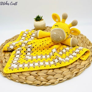 May include: A yellow and brown crocheted baby blanket with a crocheted giraffe toy on top. The blanket has a checkered pattern and the giraffe has closed eyes.