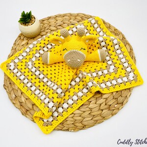 May include: A yellow and brown crocheted baby blanket with a yellow and brown crocheted giraffe toy on top. The blanket is on a woven basket.