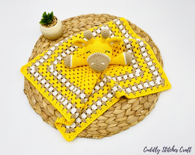 May include: A yellow and brown crocheted baby blanket with a yellow and brown crocheted giraffe toy on top. The blanket is on a woven basket.
