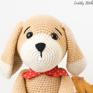 May include: A crocheted beige dog toy with white accents, black eyes, and a red polka dot bow tie.