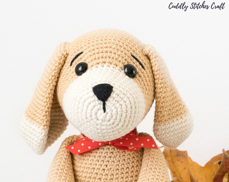 May include: A crocheted beige dog toy with white accents, black eyes, and a red polka dot bow tie.