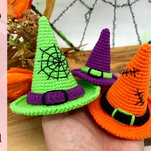 Può includere: Tre cappelli da strega all'uncinetto in verde, viola e arancione. Il cappello verde ha un disegno a ragnatela nera, il cappello viola ha una fascia verde e il cappello arancione ha cuciture nere. Ogni cappello ha una fascia nera.