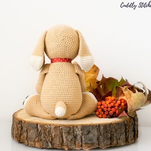 May include: A crocheted beige dog toy with white accents, sitting on a wooden slice with autumn leaves and red berries.