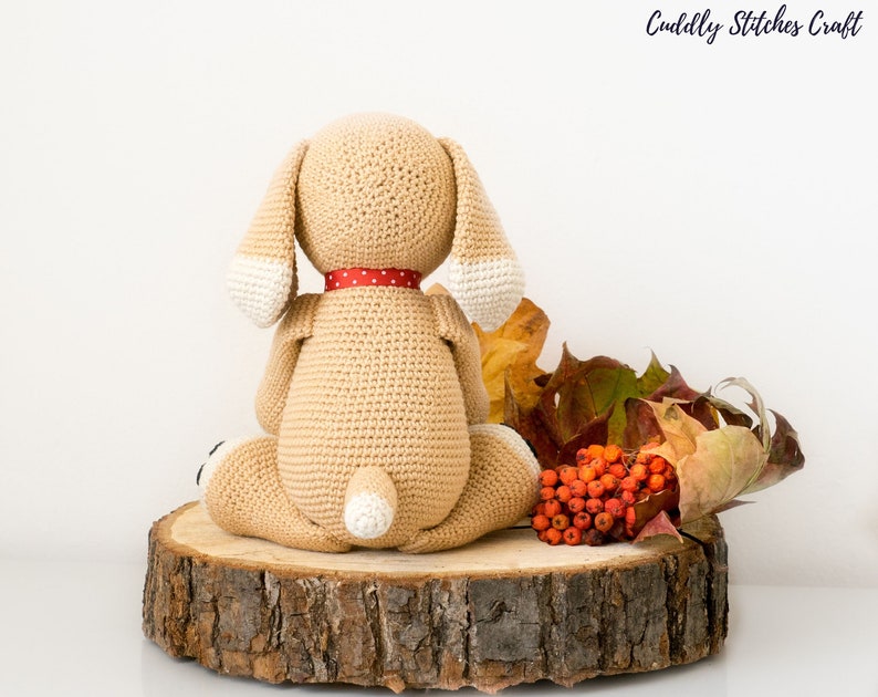 May include: A crocheted beige dog toy with white accents, sitting on a wooden slice with autumn leaves and red berries.