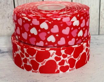 May include: Two rolls of red and white ribbon with a heart pattern. The ribbon has the word "LOVE" printed on it.