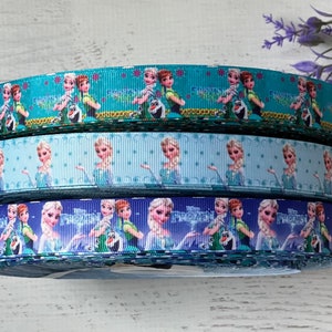 Op de afbeelding: Drie rollen blauwe en groene lint met een herhalend patroon van Frozen-karakters, waaronder Elsa en Anna. Het lint heeft de tekst "Frozen" erop gedrukt.