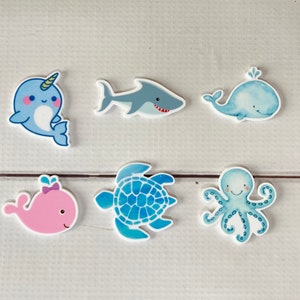 Op de afbeelding: Zes kleurrijke vilt ocean dier cut-outs. De dieren omvatten een narwal, haai, walvis, schildpad, octopus en een roze walvis.