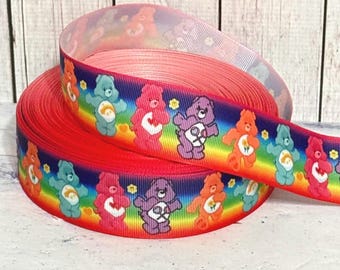 Könnte beinhalten: Rot-weiß-blaues Care Bear Band mit Regenbogenhintergrund. Das Band zeigt Care Bears mit unterschiedlich farbigem Fell und Symbolen auf ihren Bäuchen.