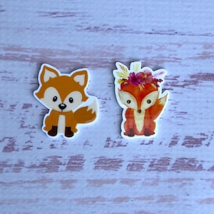 Puede incluir: Dos figuritas de zorro naranja con detalles blancos. Un zorro lleva una corona de flores.