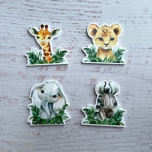 以下が含まれることがあります： ジャングルをテーマにした、カラフルな動物のステッカー4枚。ステッカーには、キリン、ライオン、ゾウ、シマウマが描かれています。それぞれの動物は緑の葉に囲まれています。