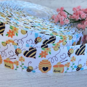 May include: White ribbon with a repeating pattern of bees, honeycombs, and hearts. The ribbon has a textured, woven look. The text "honey" appears on the ribbon.