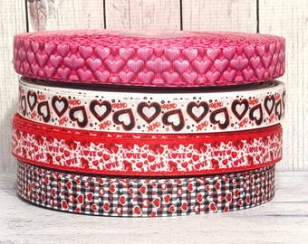 May include: Four rolls of Valentine's Day themed ribbon. The top roll is pink with white hearts, the second roll is white with black hearts and the text "XOXO", the third roll is red with white hearts and the text "LOVE", and the bottom roll is black and white gingham with red hearts.