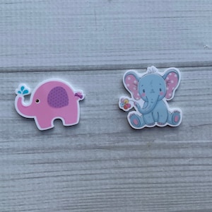 Könnte beinhalten: Zwei entzückende Elefantenaufkleber. Einer ist rosa mit einem lila Tupfenmuster und einem blauen Wasserspritzer. Der andere ist ein hellblauer Elefant mit rosa gepunkteten Ohren, der eine Blume hält. Ideal zum Basteln oder Dekorieren.