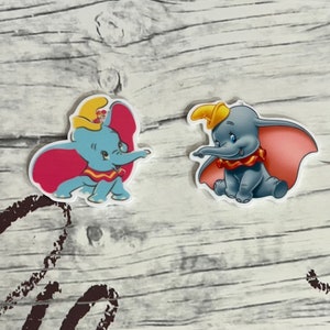 Könnte beinhalten: Zwei bunte Dumbo-Elefantenfiguren aus dem Zeichentrickfilm. Die Figuren sind aus Plastik und haben einen 3D-Effekt. Eine Figur ist blau mit einem rosa Umhang und die andere ist grau mit einem rosa Umhang.