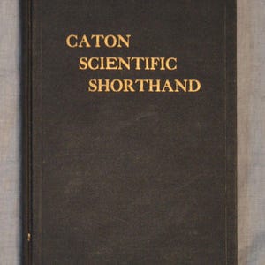May include: A rectangular hardcover book with a dark charcoal gray cover. The title CATON SCIENTIFIC SHORTHAND is printed in gold lettering on the front cover. The book features a simple, clean design with a vertical border embossed along the edge.