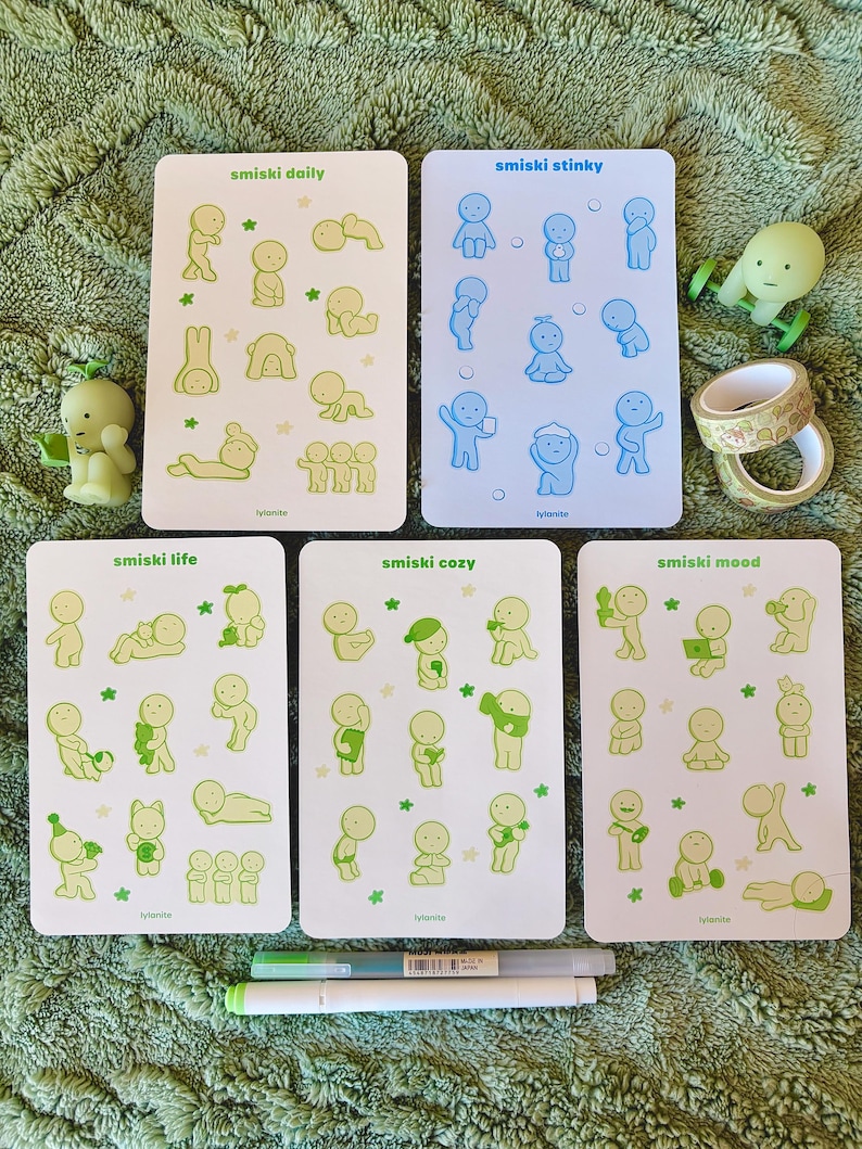 May include: A collection of Smiski figurines and sticker sheets. The sticker sheets are labeled "smiski daily", "smiski stinky", "smiski life", "smiski cozy", and "smiski mood". The figurines and stickers are in shades of green and blue.