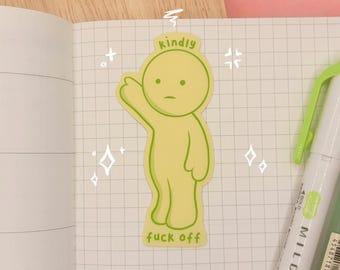 May include: A light green die-cut sticker featuring a cartoon character pointing upward with the text "kindly" above its head and "fuck off" at its feet. The sticker is placed on a grid-patterned page next to a green highlighter pen.
