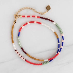 May include: Two beaded necklaces with a gold-colored chain and clasp. The necklaces feature a variety of colorful beads, including red, white, blue, green, and brown. One necklace has a small gold heart charm.