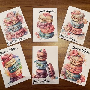 May include: Six colourful cards with watercolour illustrations of macarons and flowers. Each card has the text "Just a Note..." printed on it.